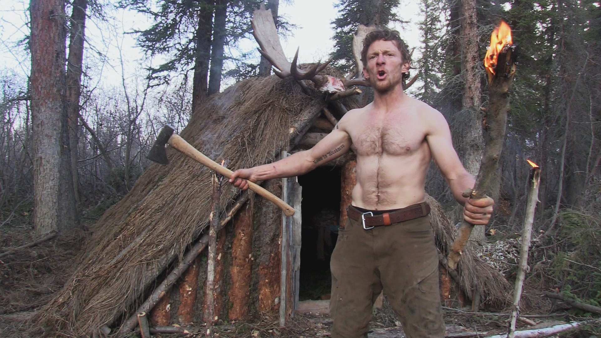 Timber Cleghorn stands shirtless in front of his shelter on the show 'Alone.'