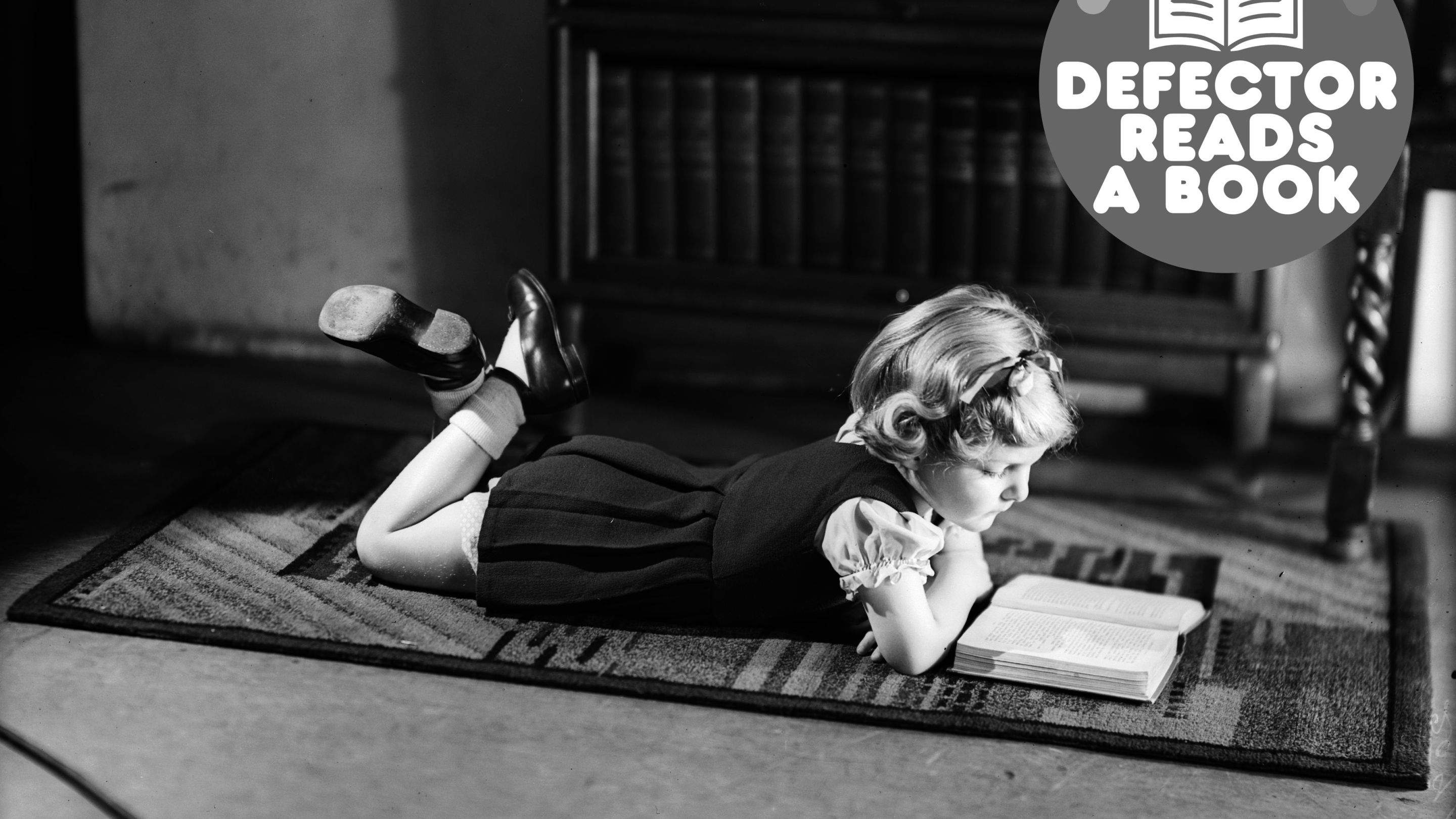 A young girl lying on a carpet while reading a book.