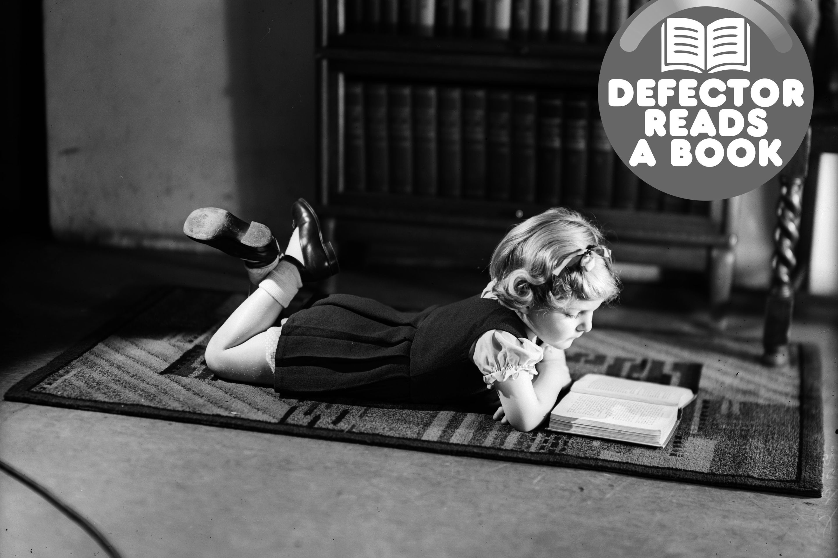 A young girl lying on a carpet while reading a book.