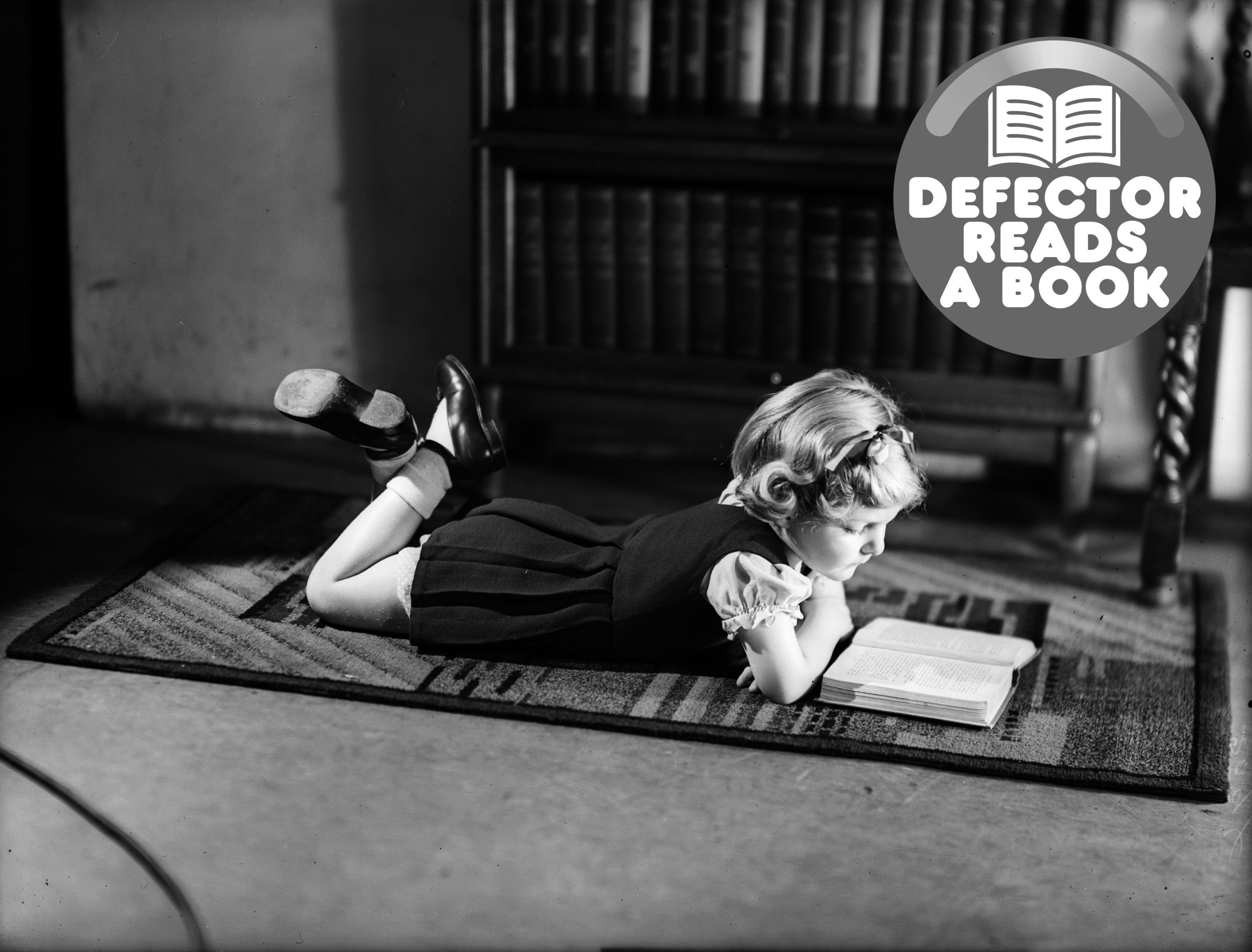 A young girl lying on a carpet while reading a book.