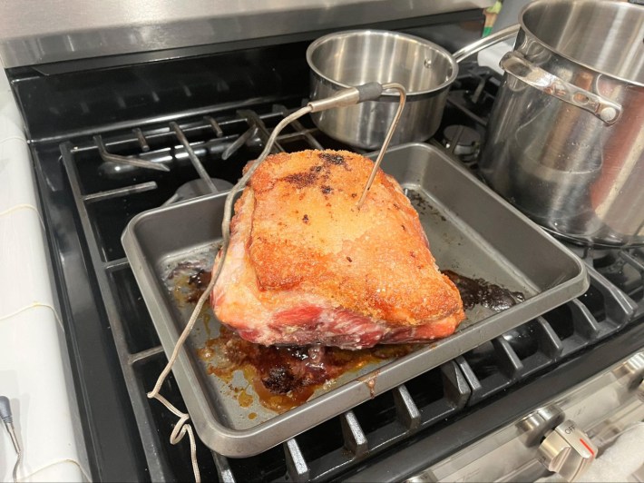 A big hunk of pork, browned from roasting, with a stainless steel probe thermometer stabbed into it.