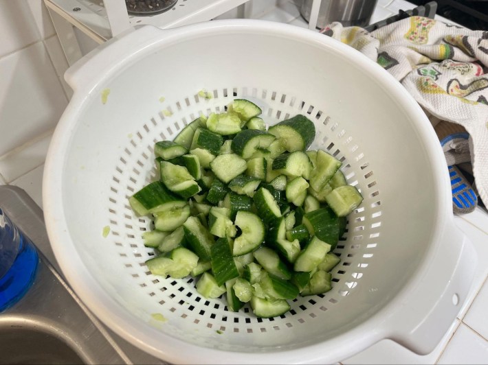 A colander with smashed chunks of cucumber filling the bottom.