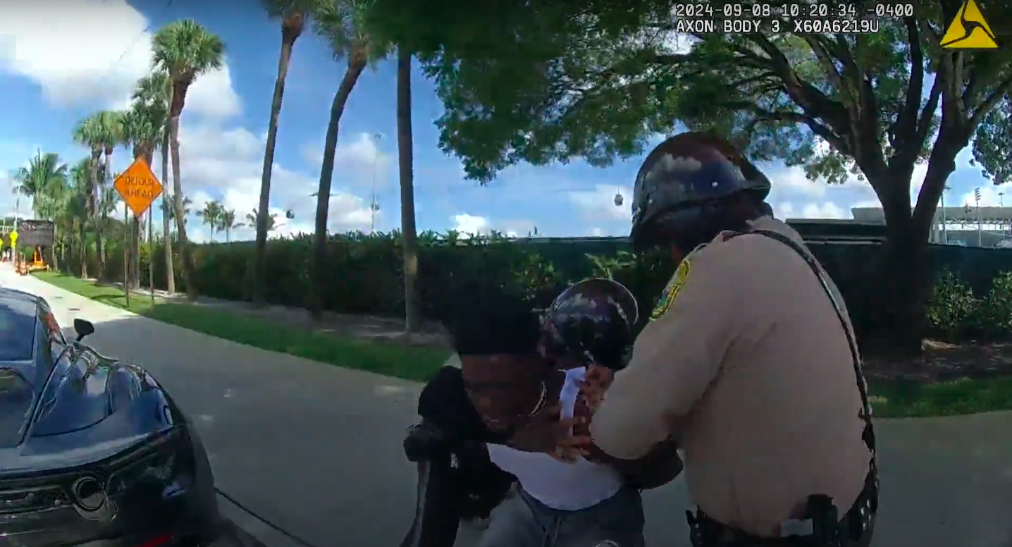 A Miami-Dade police officer grabs Tyreek Hill from behind during his detainment