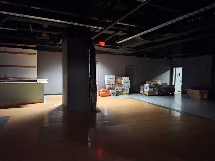 An empty store in the former Playground mall in which someone is storing a bunch of boxes of vegetables in the corner.