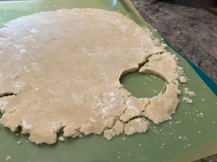 A hole cut in a sheet of shortbread dough, which has cracked.