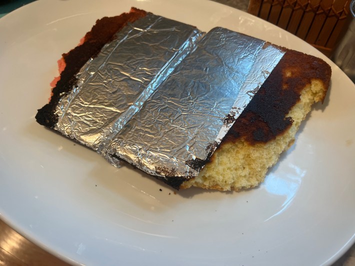 Aluminum foil clings to the bottom of two broken, badly burned cake sponges.