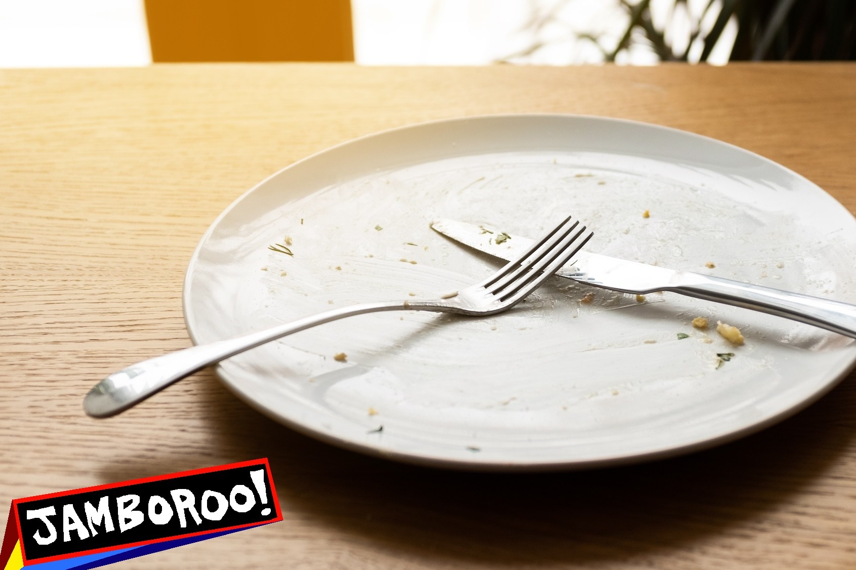 A dirty empty plate, fork and knife on a wooden table. Used cutlery, symbolizing the end of lunch or dinner.