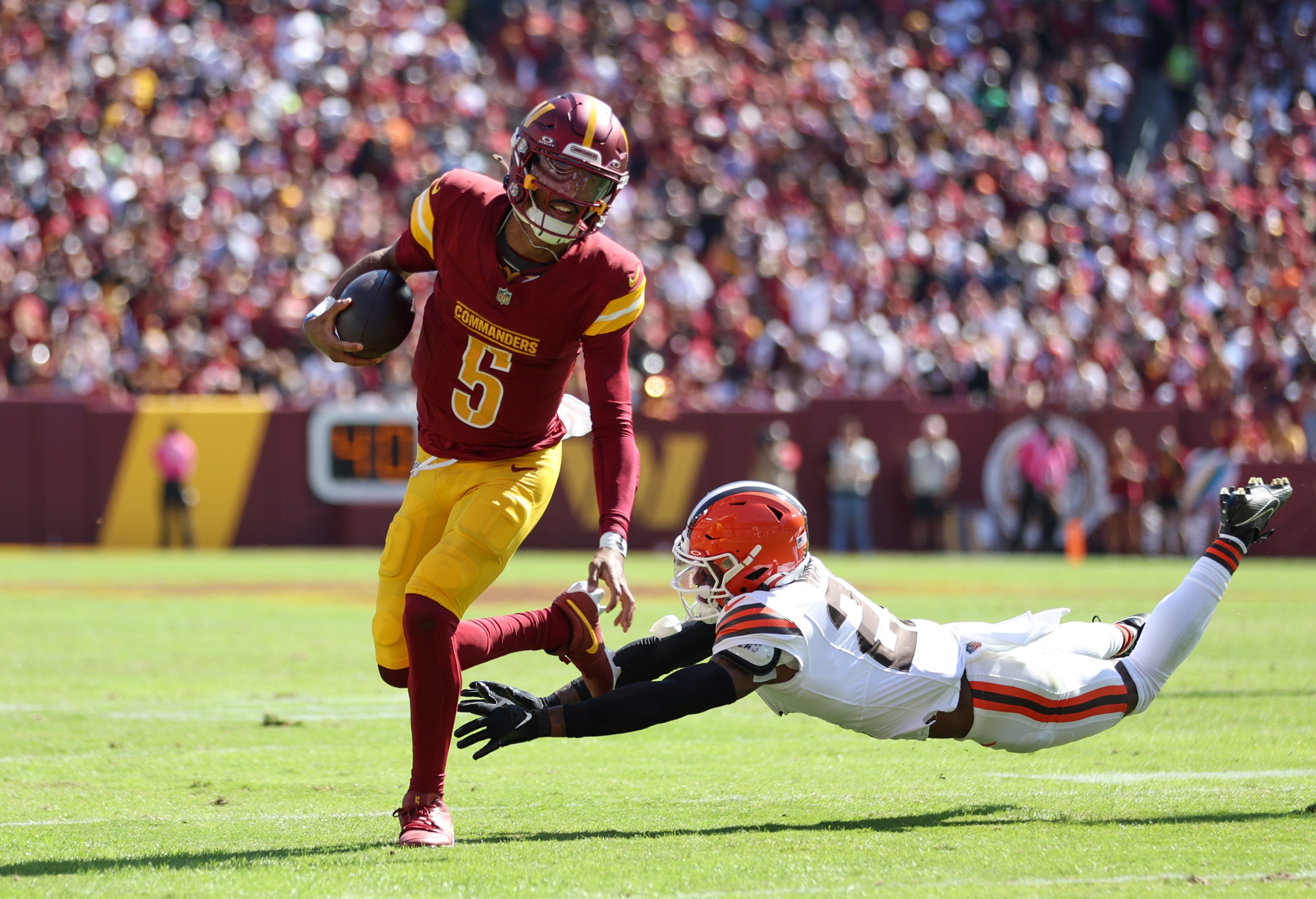 Jayden Daniels #5 of the Washington Commanders runs the ball as Denzel Ward #21 of the Cleveland Browns attempts to tackle during the first half at FedExField on October 06, 2024 in Landover, Maryland.