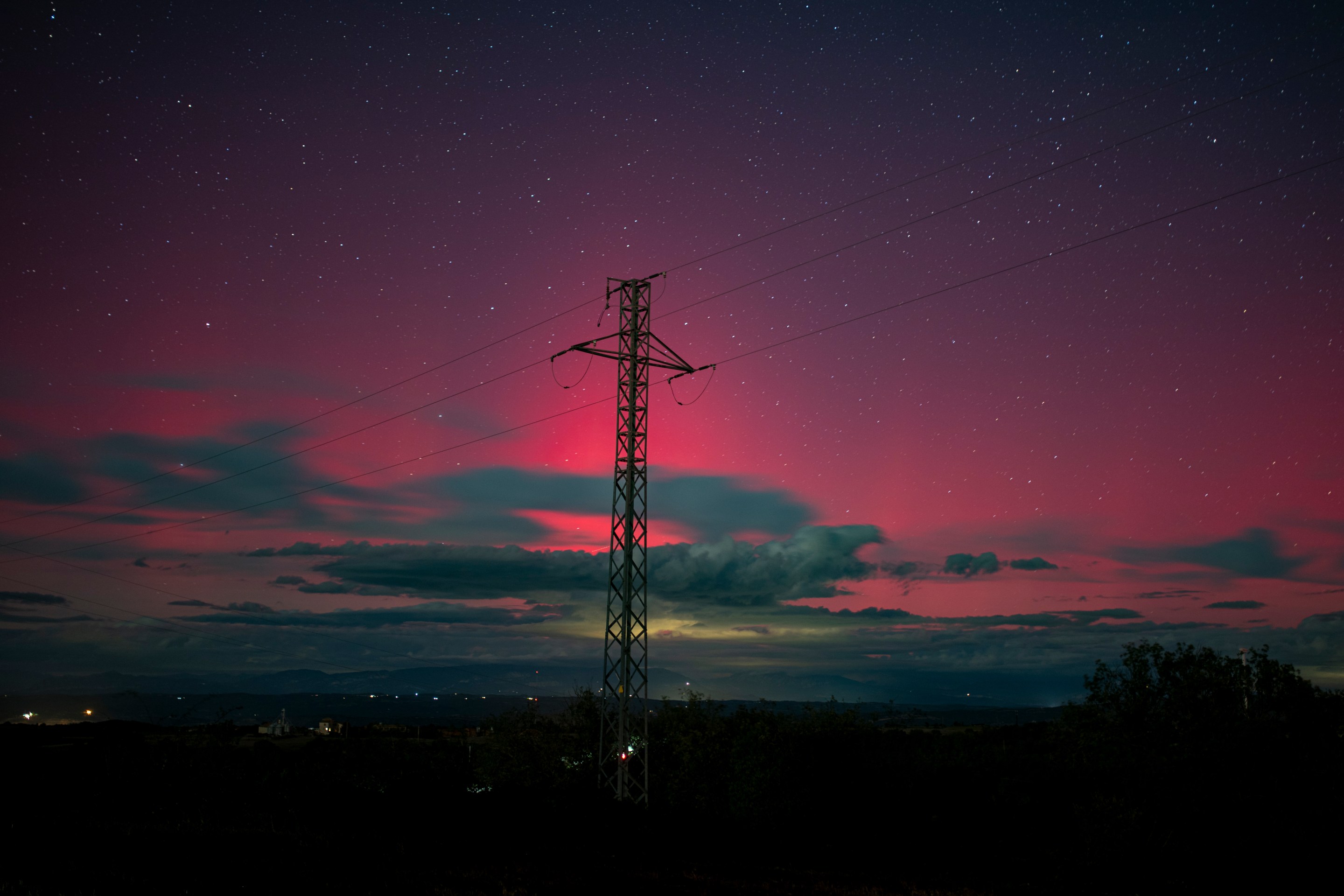 Northern lights are seen across a night sky; in the foreground, there's a telephone tower