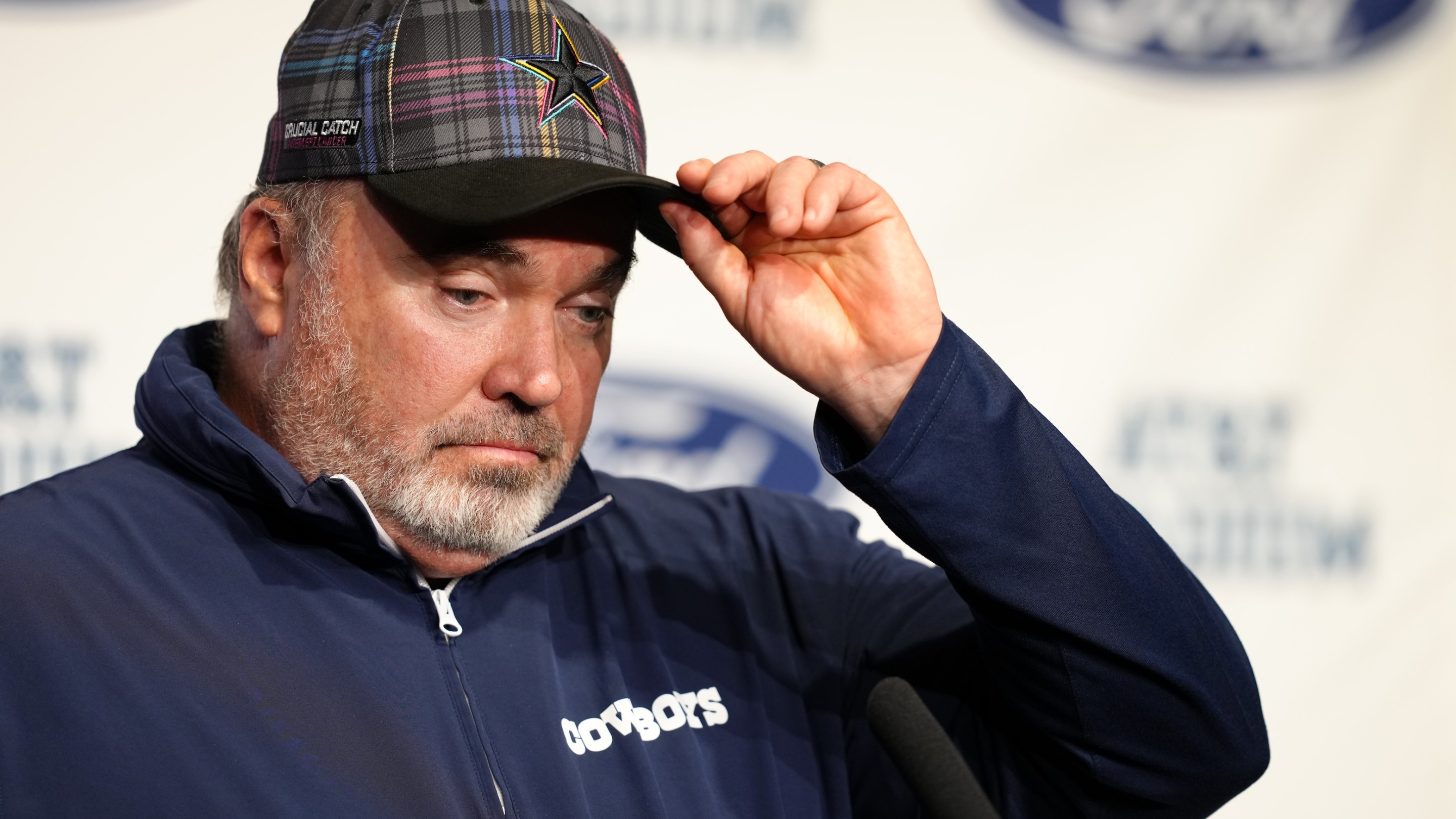 Dallas Cowboys head coach Mike McCarthy speaks to media at a press conference after the game against the Detroit Lions on October 13, 2024. He is wearing a plaid Cowboys hat and looks exhausted.