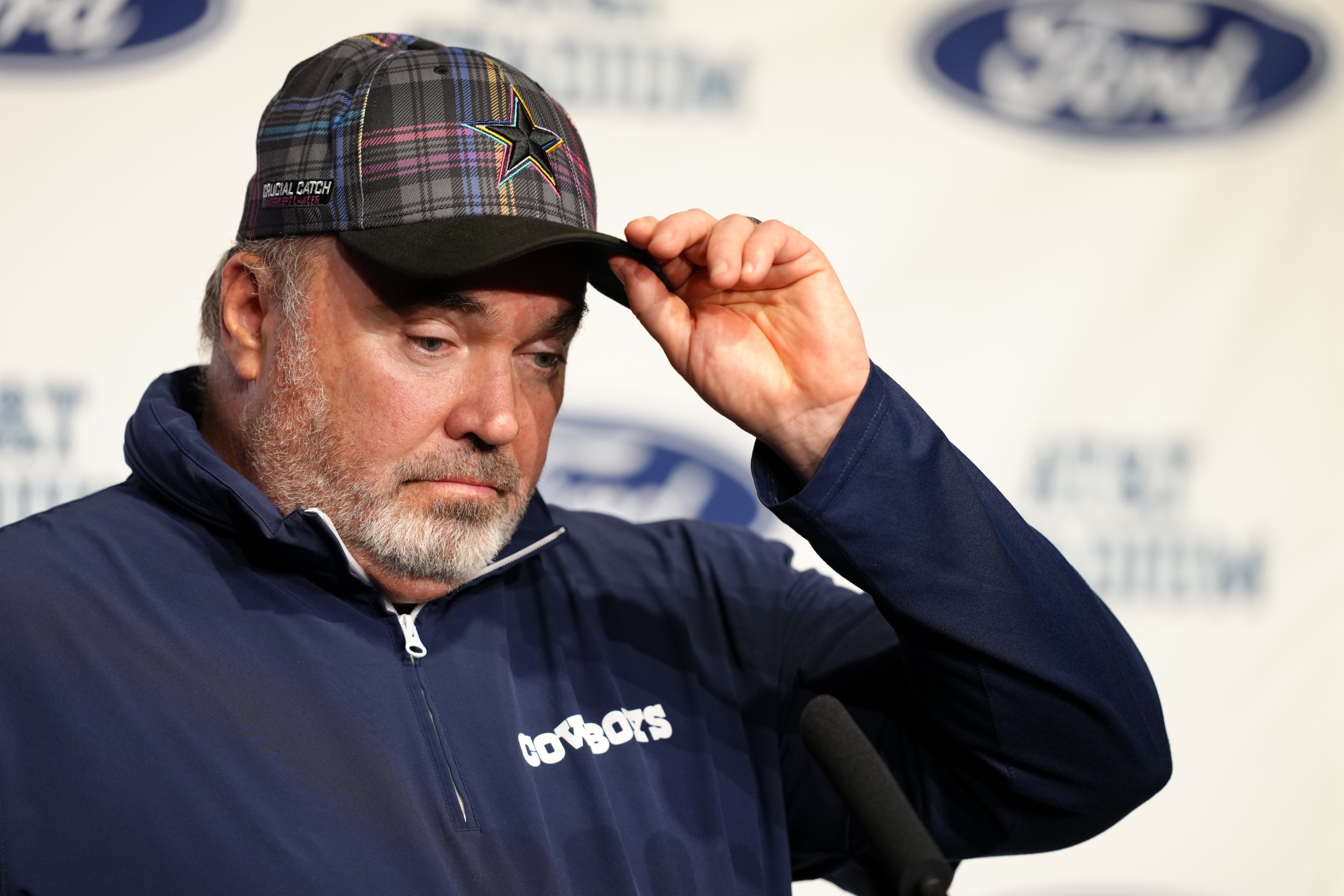 Dallas Cowboys head coach Mike McCarthy speaks to media at a press conference after the game against the Detroit Lions on October 13, 2024. He is wearing a plaid Cowboys hat and looks exhausted.