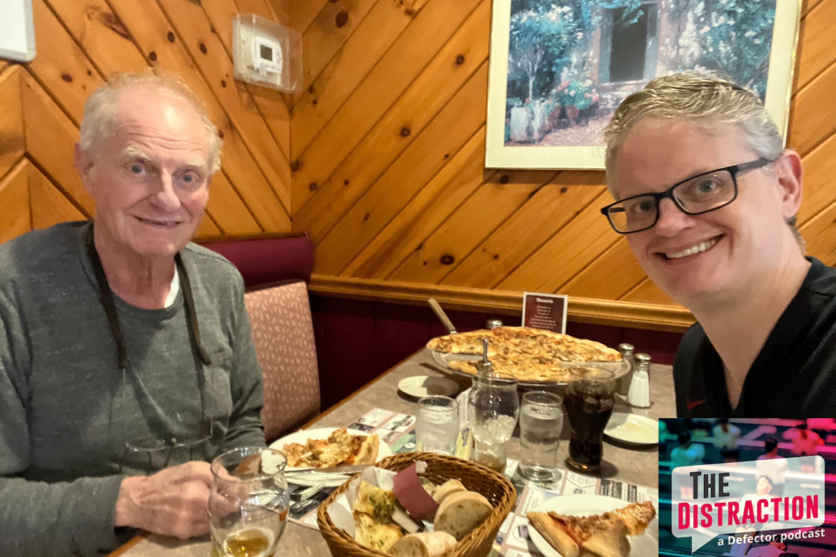 Drew and his father at a pizzeria together. Drew's on the right, smiling; his father is on the left, also smiling, looking like an older version of Drew. There's some pretty solid looking pizza in the middle.