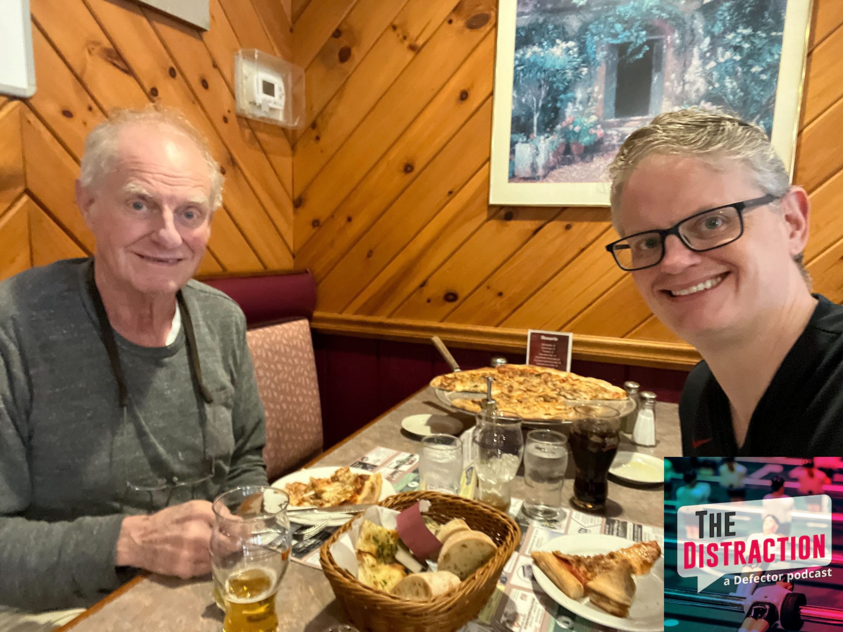 Drew and his father at a pizzeria together. Drew's on the right, smiling; his father is on the left, also smiling, looking like an older version of Drew. There's some pretty solid looking pizza in the middle.