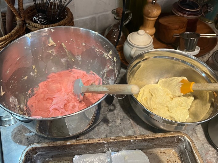 Two mixing bowls, one with pink batter and one with white.