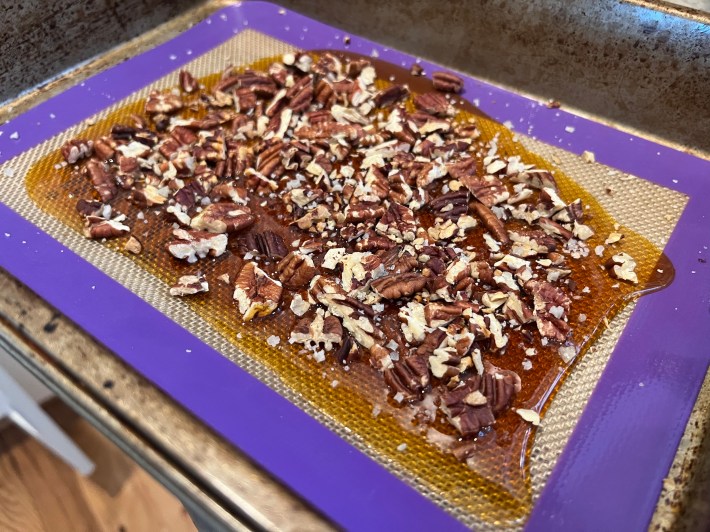 Caramel toffee spread on a silicone mat, topped with pecans and sea salt.