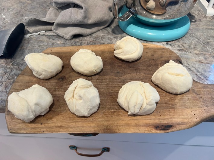 Seven roughly equal balls of bread dough on a wood cutting board.