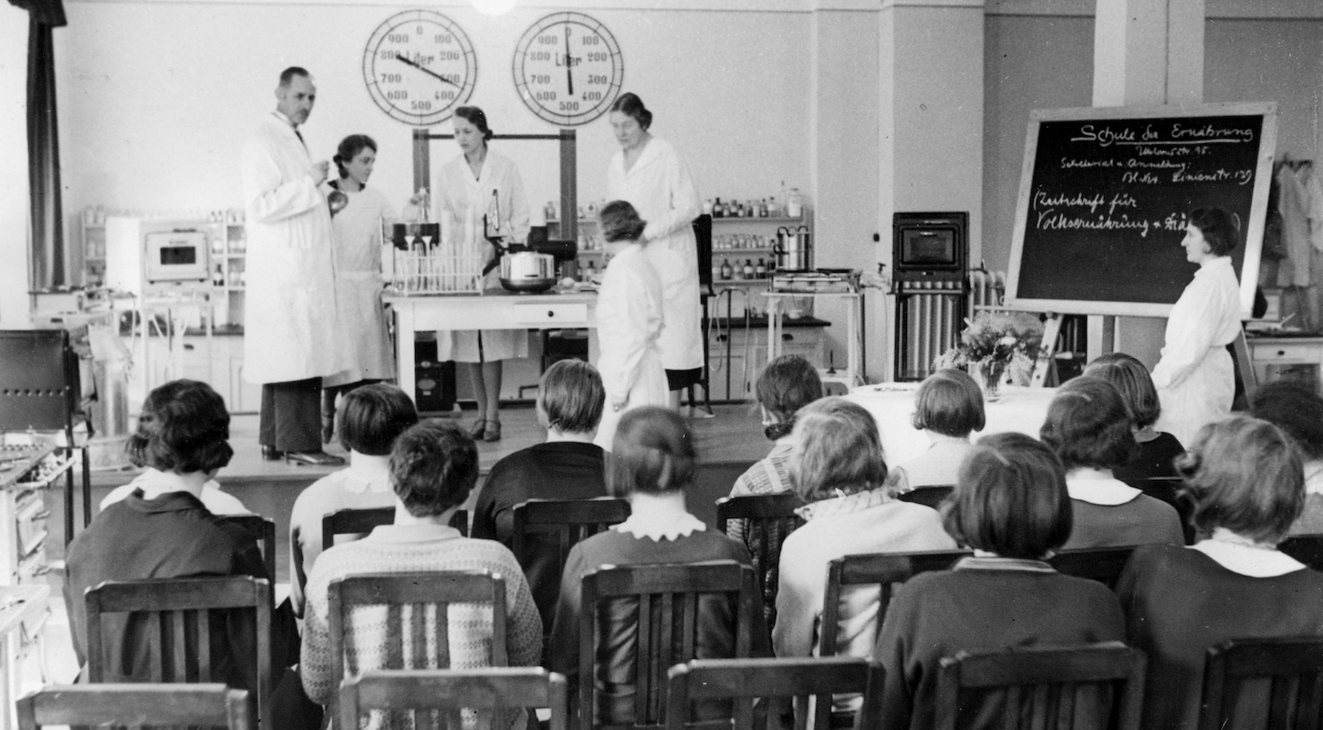 Students observe a classroom demonstration in an old black-and-white photograph from the 1930s.