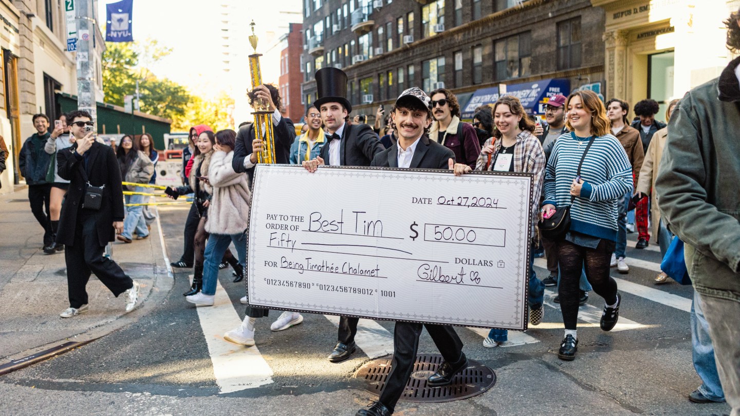 a large group is led by a man carrying a giant check