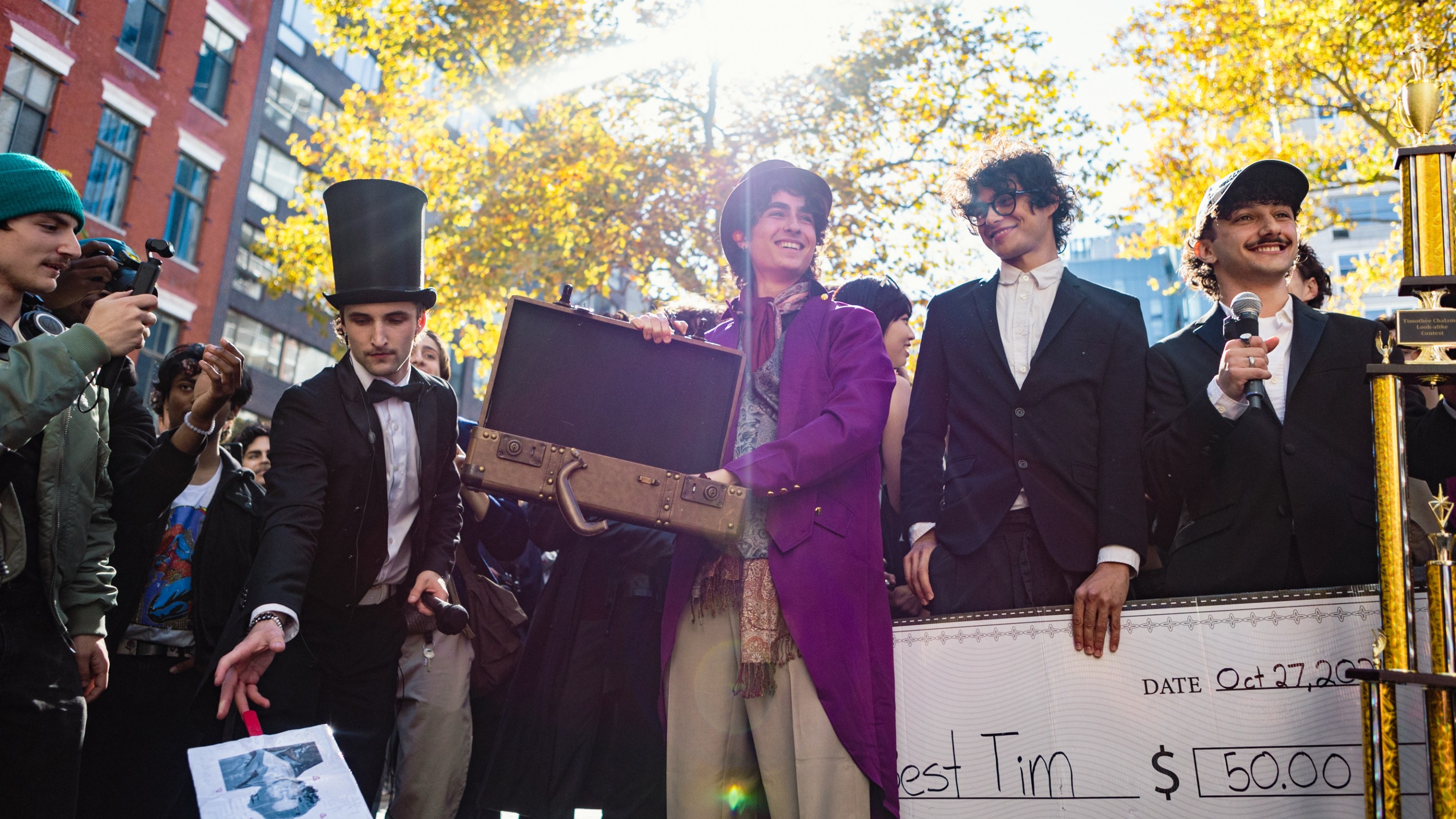 A Timothee Chalamet lookalike in a Wonka costume showcases an empty briefcase