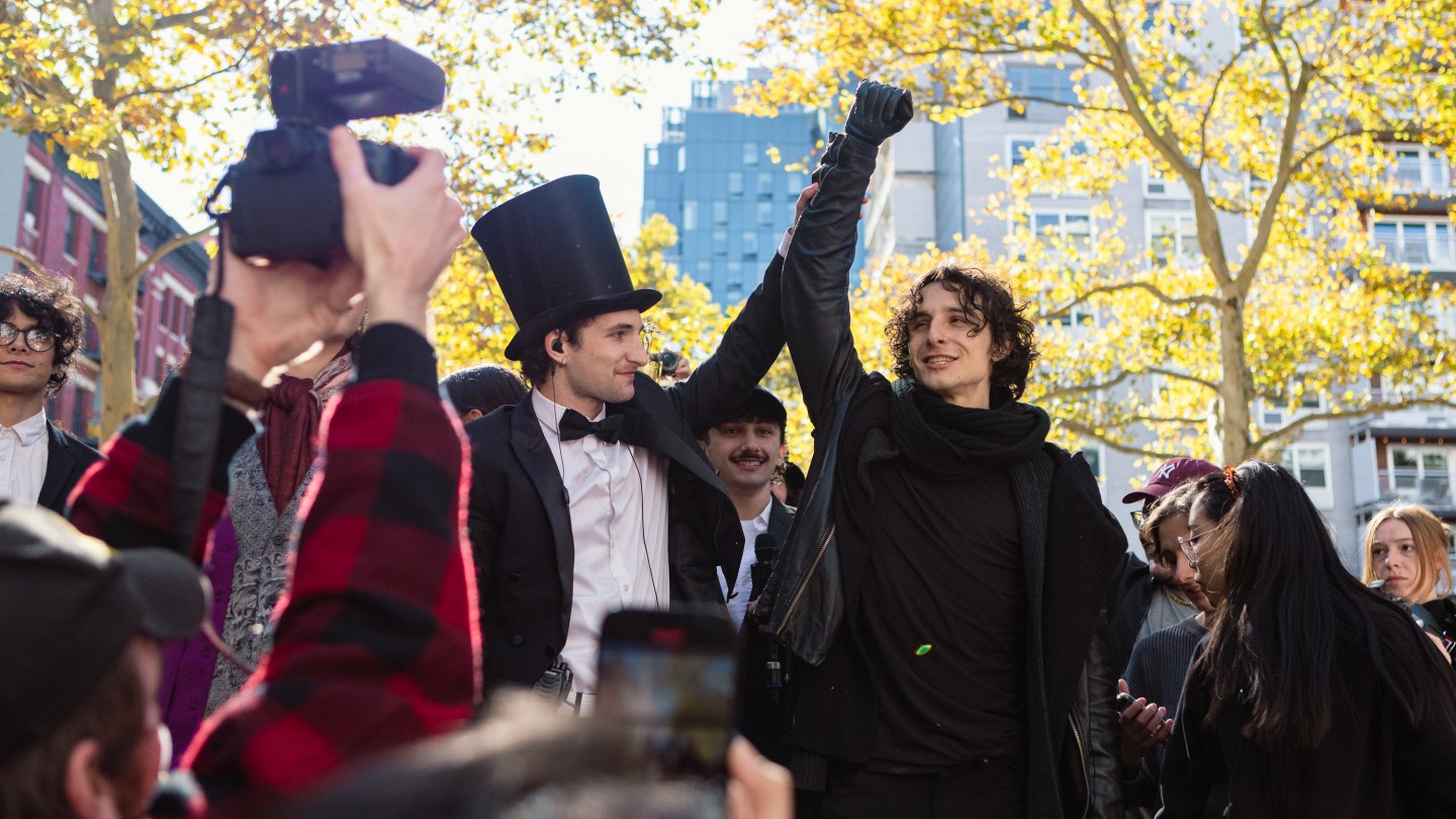 A Timothee dressed in a Dune costume has his hand raised