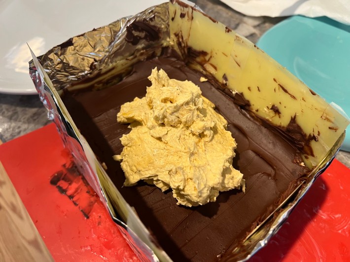 A blob of buttercream sits on top of ganache spread inside a makeshift cake frame.