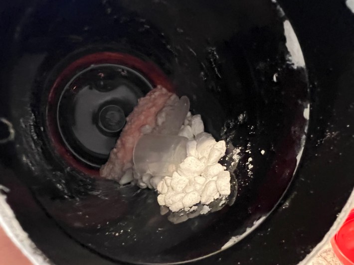 Crystallized chunks of white creatine powder, inside a black plastic container.