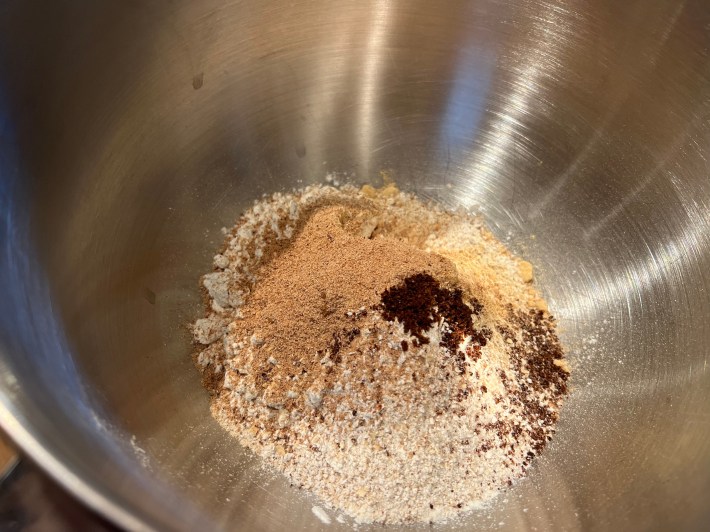 Flour, ground oatmeal, ground ginger, ground cinnamon, ground clove, and grated nutmeg, in a large mixing bowl.