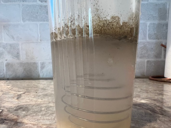 Brown powder of fermented greens settle on the surface of water inside a shaker bottle.