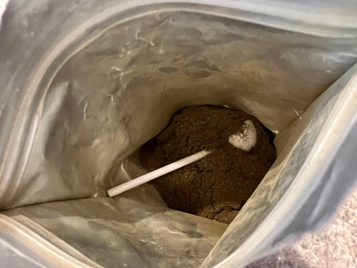 Brown powder of fermented greens, inside a bag, with a scoop.