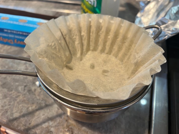A coffee filter rests inside a mesh sieve, over a mixing bowl.