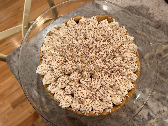 A top-down view of a completed Banoffee pie, topped with Chantilly cream and grated chocolate.