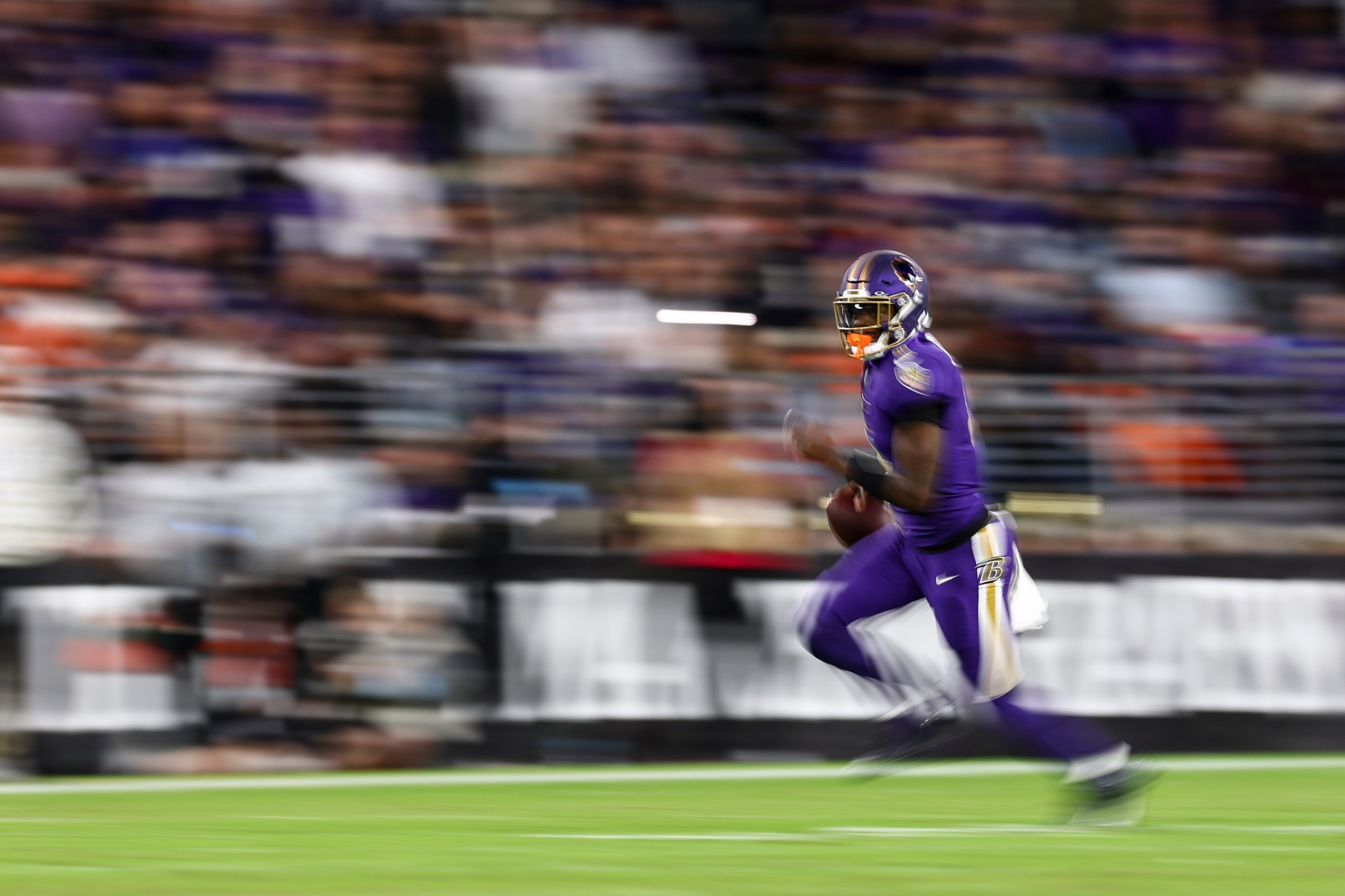 Lamar Jackson of the Baltimore Ravens carries the ball during the first half of an NFL football game against the Cincinnati Bengals. The image is blurry in an artful way.