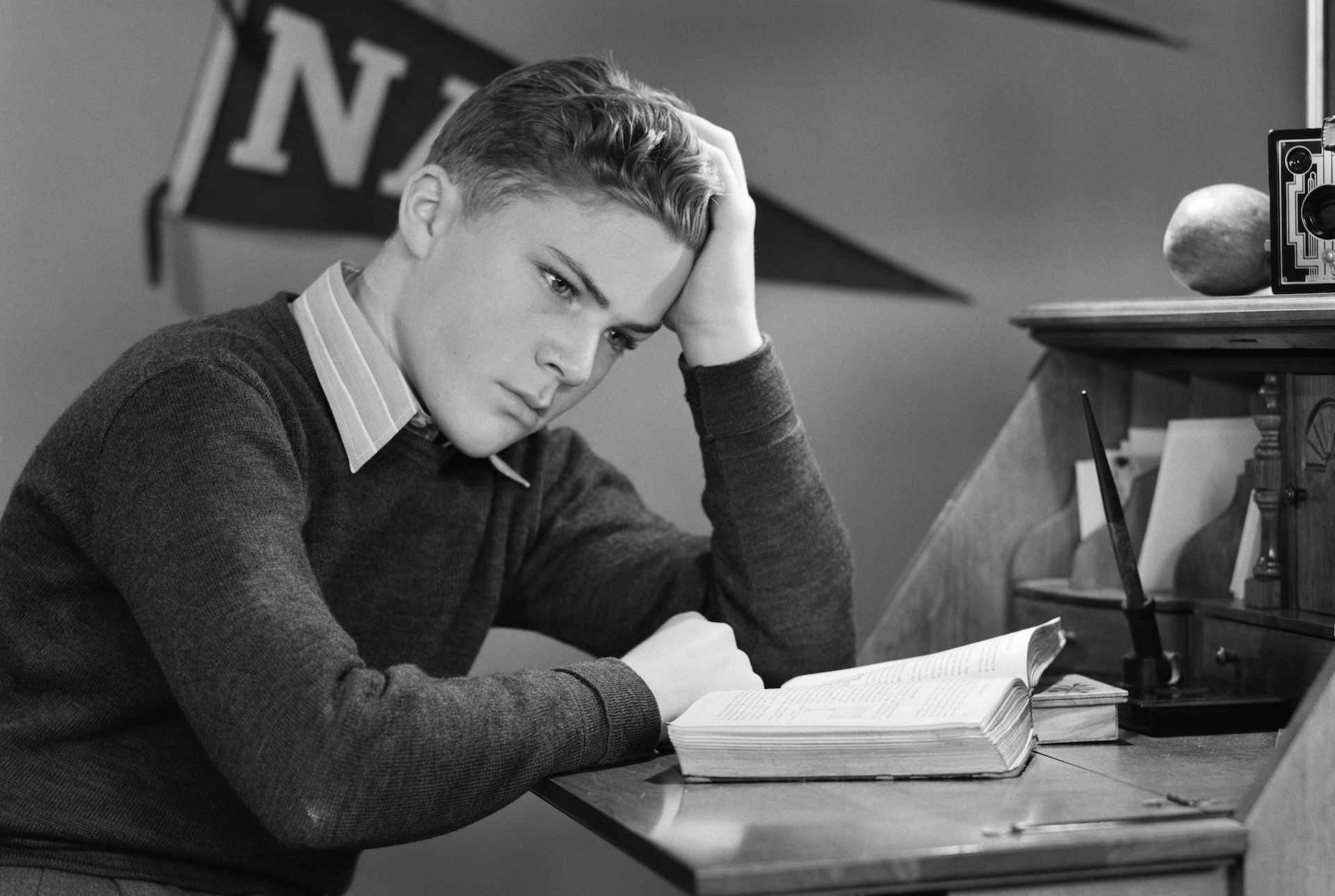 1940s YOUNG BOY STUDYING IN ROOM WITH ARMY NAVY PENNANTS ON WALL