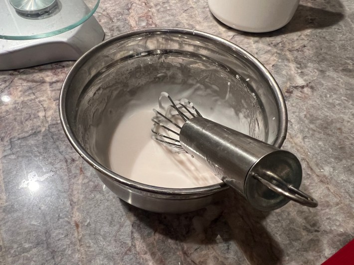 White glacé icing in a bowl, with a whisk.