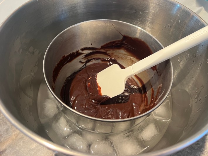 Melted chocolate glaze sits in a mixing bowl, inside a larger bowl filled with ice and water.