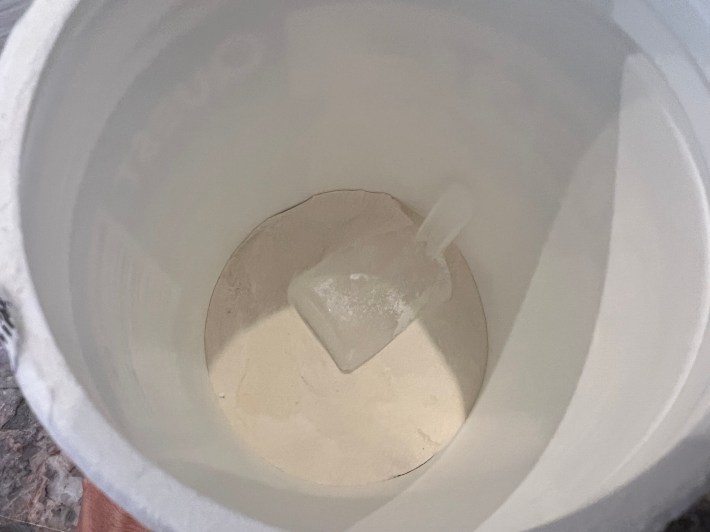 White vanilla-flavored protein powder, inside a plastic container, with a scoop.