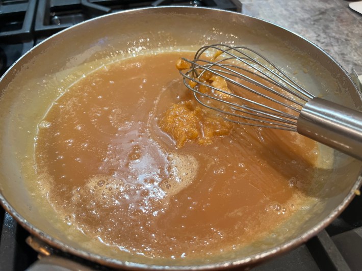 Hardened, clumped caramel in a pan, with an overmatched whisk.