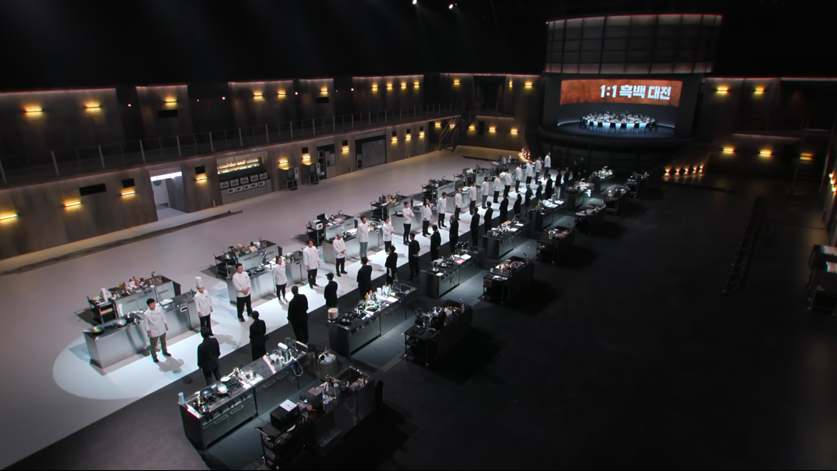 A cooking arena is divided into two sides: one black and one white. On each side there are ten chefs facing the other side.