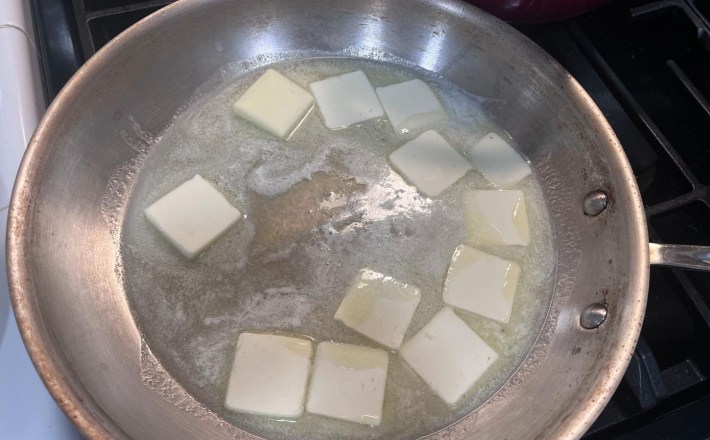 Pats of butter melting in a stainless steel pan.