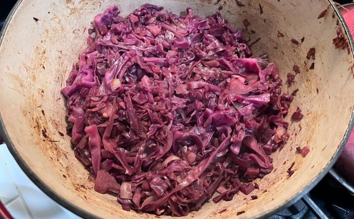 A dutch oven–type vessel with cooked purple cabbage in it. The cabbage has softened and reduced from its raw state the diced apples appear to have all but totally disintegrated into the cabbage.