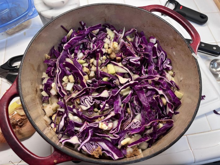 A dutch oven–type vessel with raw purple cabbage, diced apple, and other ingredients in it.