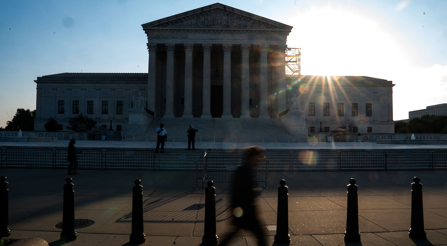 The U.S. Supreme Court building with the low afternoon sun behind it and a pedestrian in the foreground.