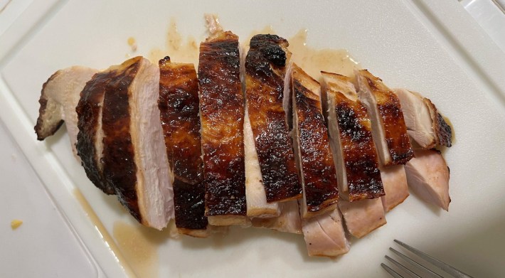 A roasted turkey breast, sliced across the grain into 10 slices, each with a strip of the crispy skin still atop them.