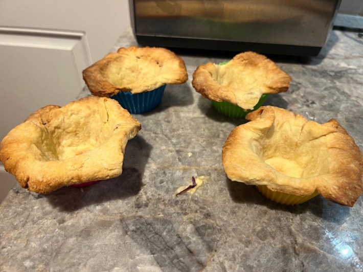 Four tart crusts, baked and trimmed and showing some damage.