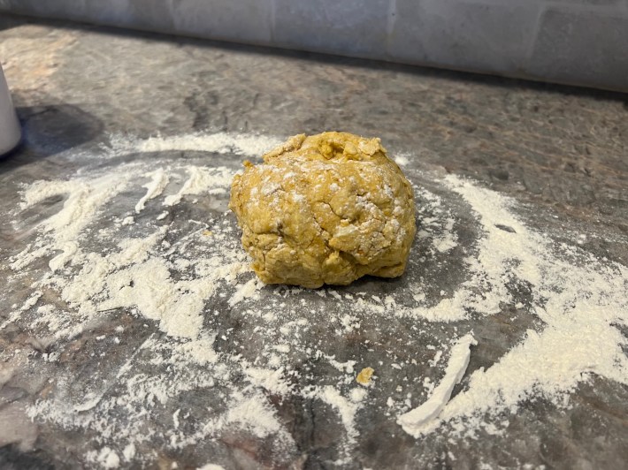 A gnarly-looking lump of pre-kneaded bread dough sits on a floured surface.