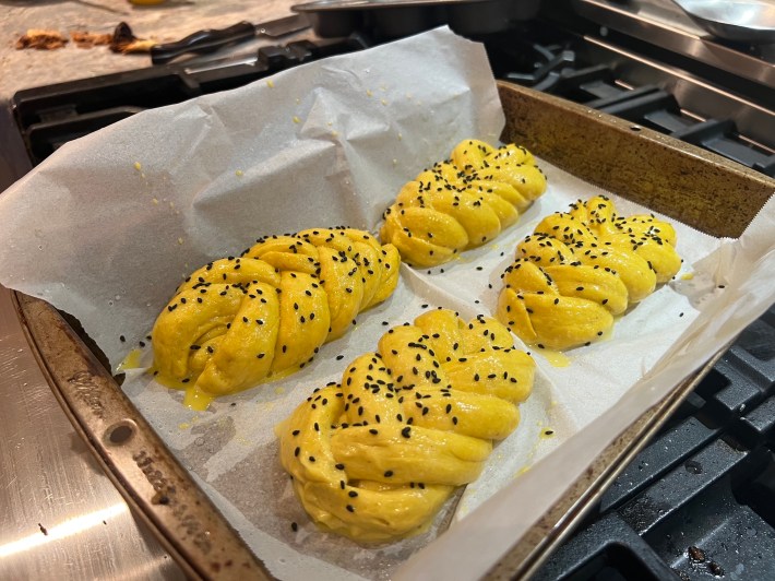 Four plaited buns, washed in egg and dressed with sesame seeds, wait to go into the oven.