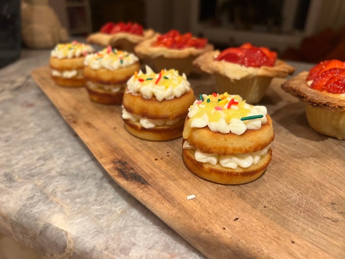 A close view of a completed lemon sandwich cake, with cream-cheese icing, piped lemon curd, and sprinkles.