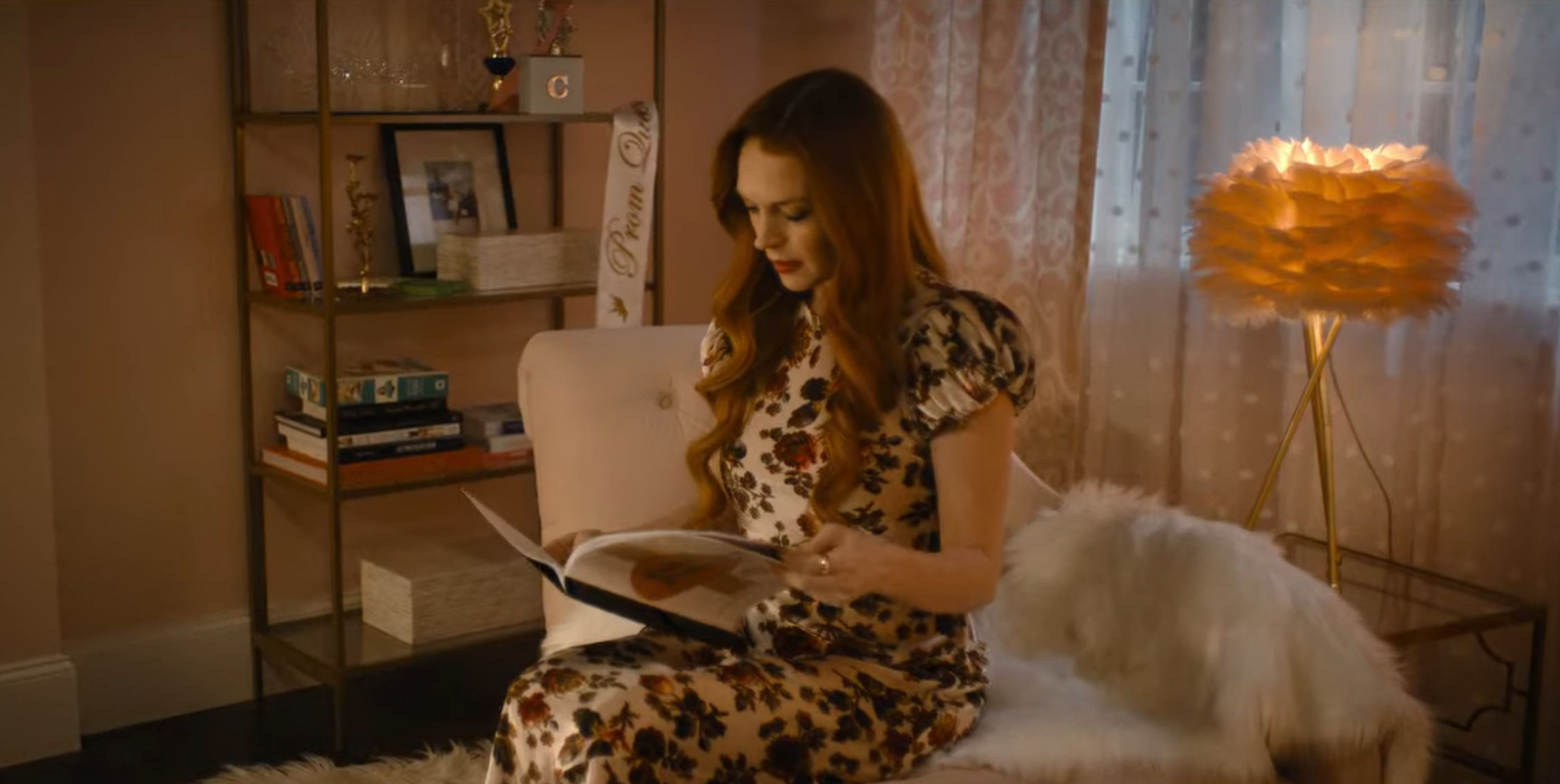 Lindsay Lohan sitting on a chair opening a book that reads "Construction Proposal Lifestyle Complex"