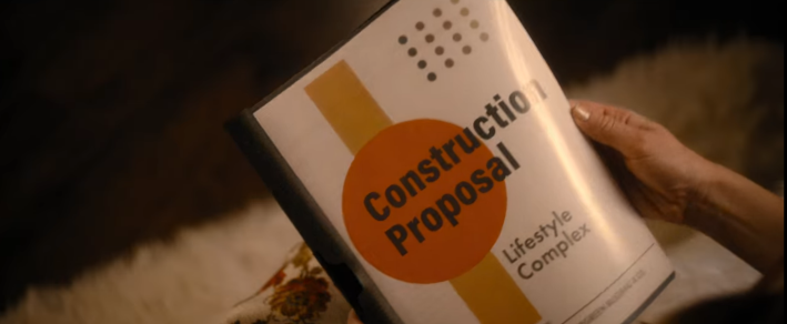 A still from the Netflix movie Our Little Secret that shows Lindsay Lohan's hand holding a booklet called "Construction Proposal" along with a subheading that reads "Lifestyle Complex"