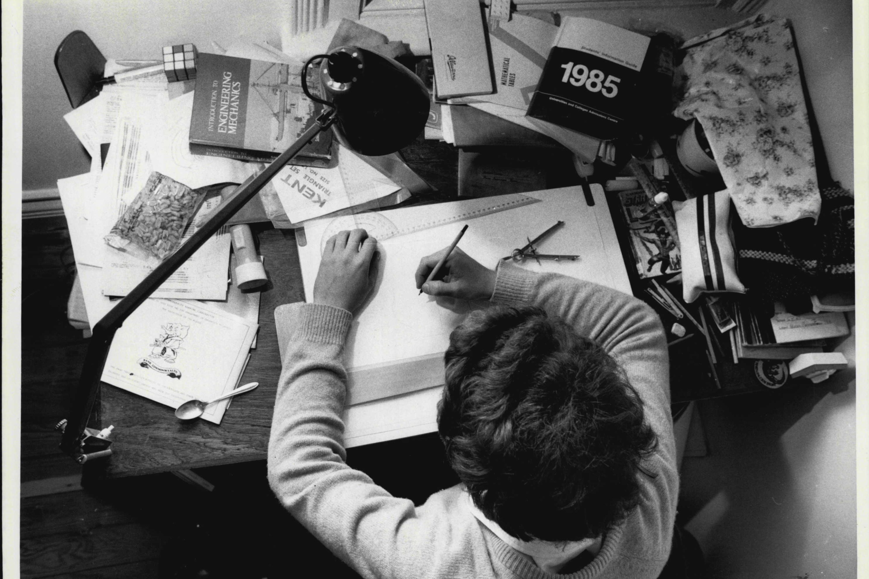 A person sits at a desk filled with books and writes in a notebook.